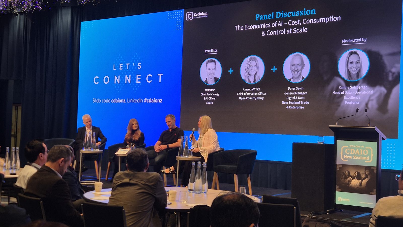 The CDAIO New Zealand panel on stage, from left Peter Gavin, Amanda White, Matt Bain and moderator Xanthe Sulzberger, under a screen showing the session title The Economics of AI, Cost, Consumption and Control at Scale