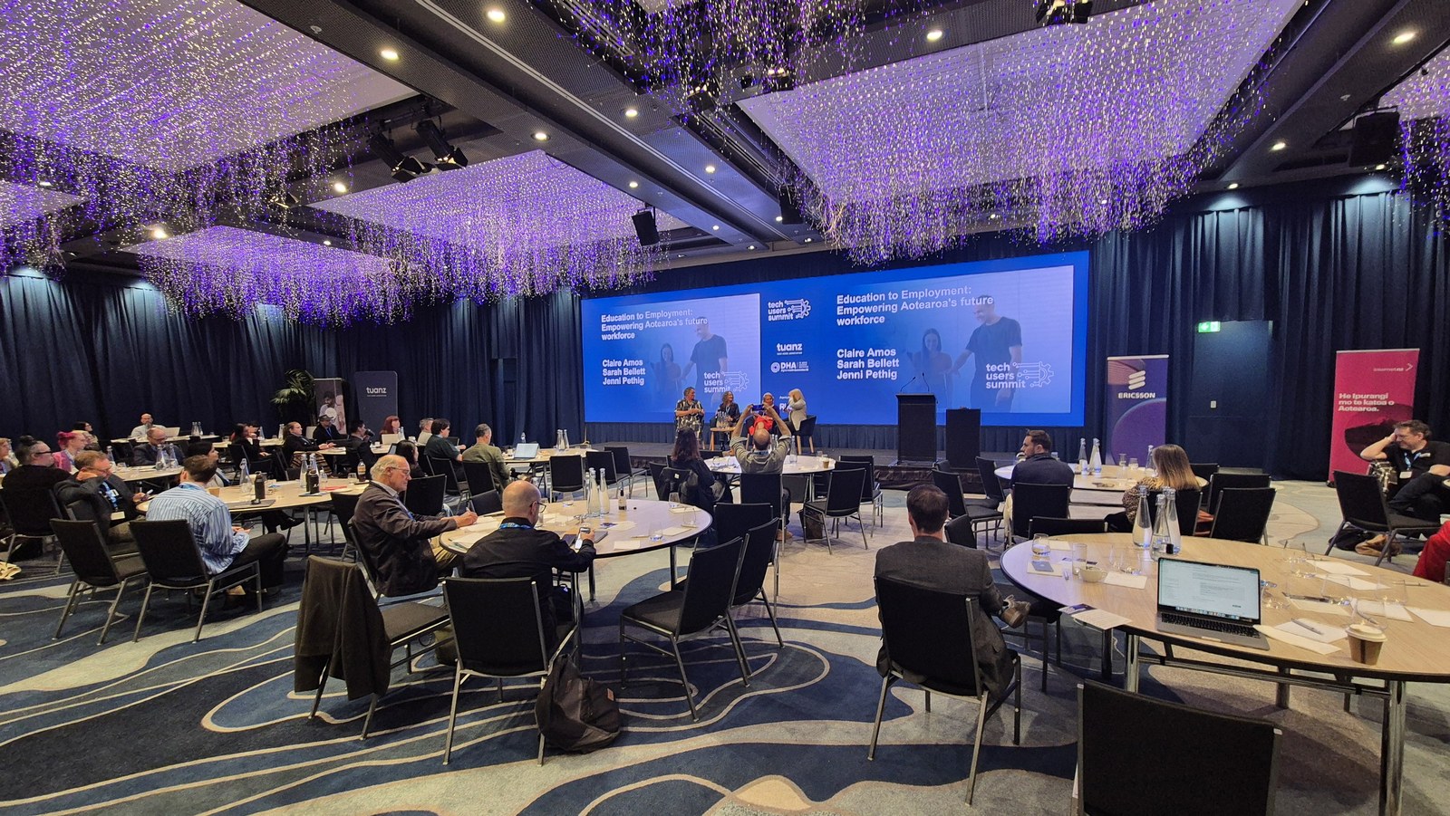 The Tech Users Summit room during the Education to Employment session, delegates seated at round tables facing the stage