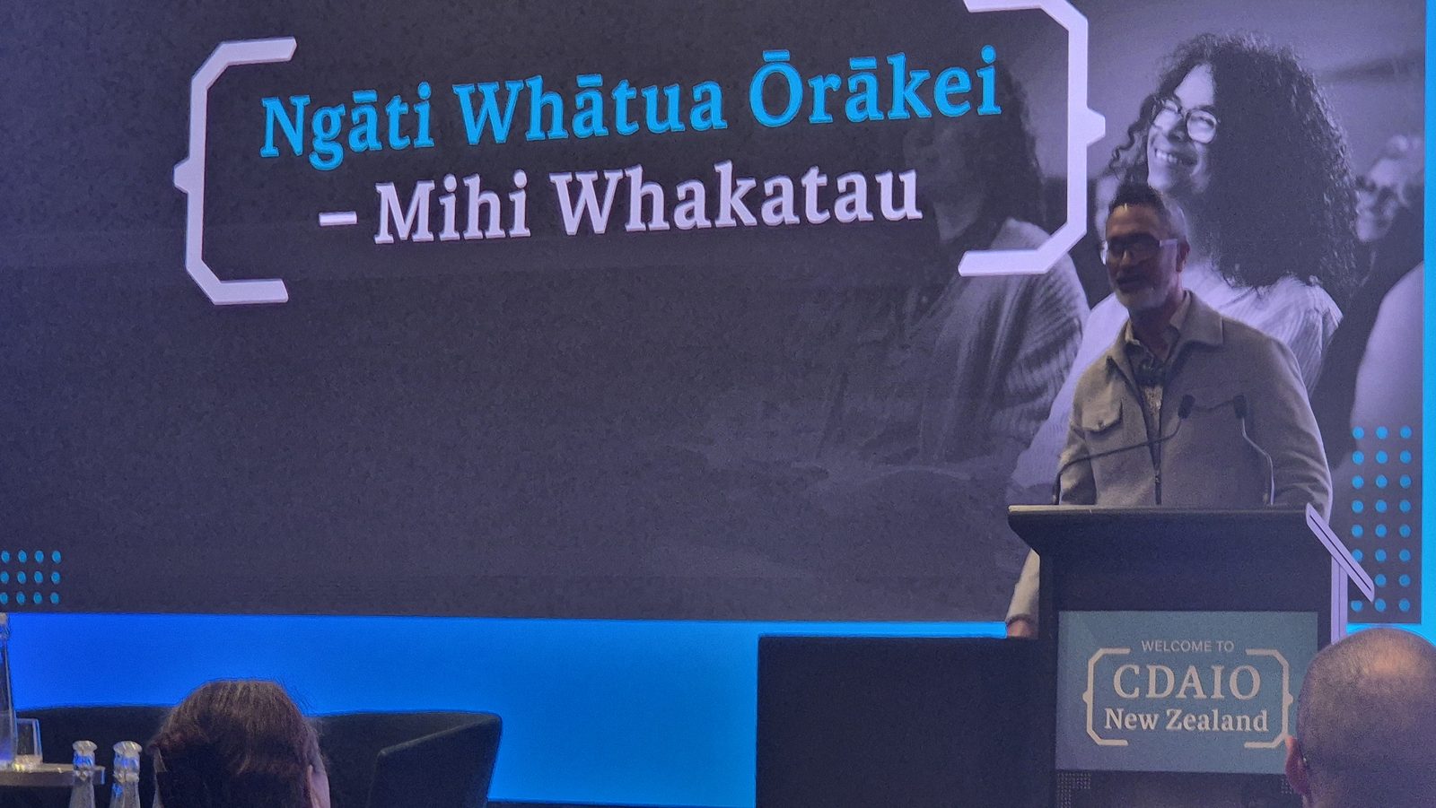 Te Aroha Grace speaking at a lectern marked Welcome to CDAIO New Zealand, under the session title Ngāti Whātua Ōrākei, Mihi Whakatau