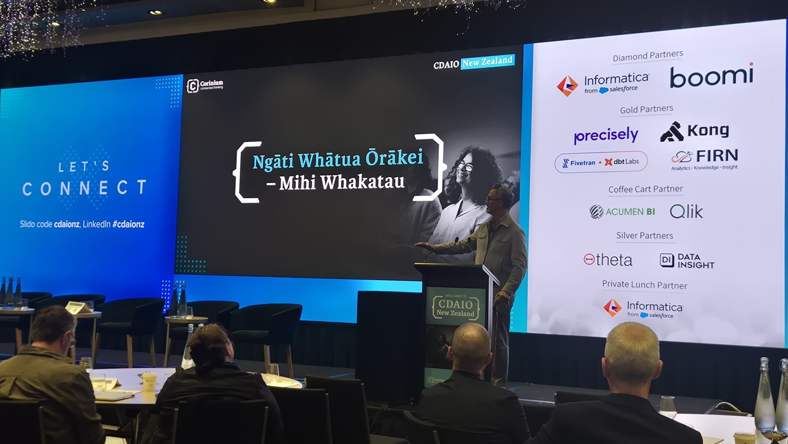 Te Aroha Grace at the lectern on the CDAIO New Zealand stage, beside a screen reading Ngāti Whātua Ōrākei, Mihi Whakatau, with delegates seated at tables in the foreground